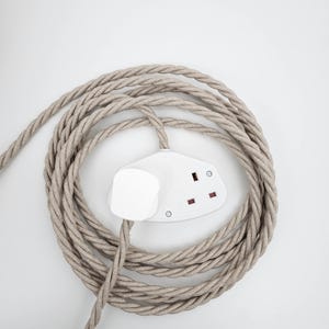 May include: A white electrical socket with a beige braided cable wrapped around it.