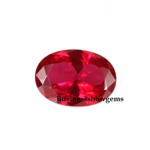 May include: A vibrant red oval-shaped gemstone with a faceted cut. The gemstone is set against a white background.