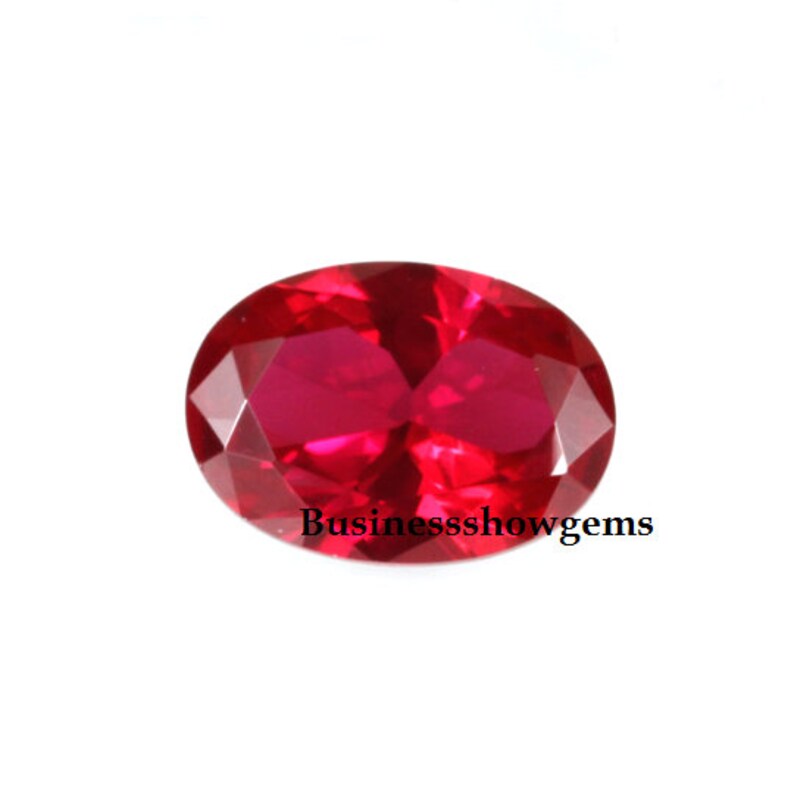 May include: A vibrant red oval-shaped gemstone with a faceted cut. The gemstone is set against a white background.