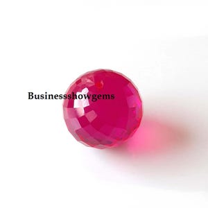 Op de afbeelding: Een facetgeslepen, ronde, felroze edelsteen kraal met een geboord gat. De kraal heeft een geometrisch patroon van driehoekige facetten. De tekst "Businessshowgems" is zichtbaar in de afbeelding.