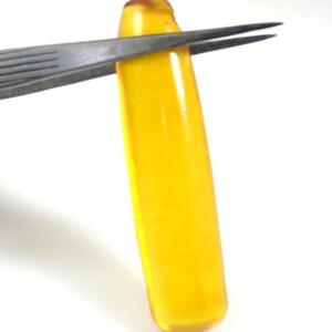 May include: A bright yellow, translucent, elongated, oval-shaped object with rounded ends. The object is being held by a pair of tweezers.