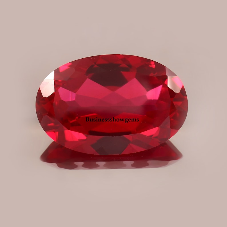 May include: A vibrant red oval-shaped gemstone with a high polish. The gemstone is faceted and reflects light beautifully.