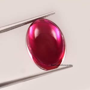 May include: A vibrant red oval cabochon gemstone with a high polish. The gemstone is set in a silver tone setting and is ready to be used in jewelry making.