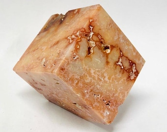 May include: A cube-shaped decorative stone with a mix of peach, cream, and gold colors. The stone has a natural, textured appearance with visible veins and patterns. The cube is displayed on a white surface.