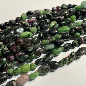 May include: A strand of green and black gemstone beads. The beads are smooth and oval-shaped. They are strung on a clear thread.