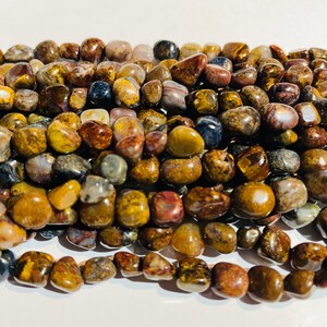 May include: A close-up of a collection of polished gemstones in shades of brown, yellow, and grey. The stones are smooth and rounded, likely for jewellery or crafts. The gemstones are strung together, ready for use.