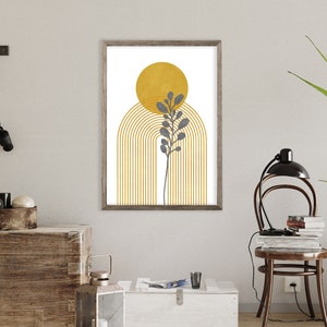 May include: A framed print with a minimalist design featuring a yellow sun, a gray plant, and a gold archway. The print has a white background and is framed in a light brown wood frame.