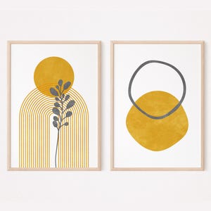 May include: Two framed abstract art prints. One features a yellow sun shape above a gray plant and a yellow arched design. The other print has a gray circle above a yellow oval shape. Both are on a white background.