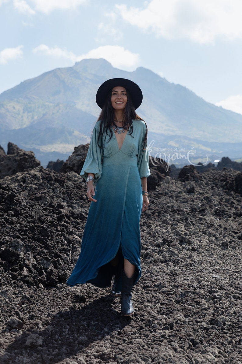 Puede incluir: Un vestido largo de manga larga con un degradado de color que va del verde salvia claro en el corpi&ntilde;o al verde azulado oscuro en el dobladillo, con escote en V profundo, cintura entallada y falda cruzada. Incluye el texto Organic clothing Kayam&eacute;.