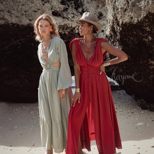 Puede incluir: Dos mujeres con vestidos largos est&aacute;n de pie en una playa de arena. La mujer de la izquierda lleva un vestido verde claro con una hebilla de cintur&oacute;n grande. La mujer de la derecha lleva un vestido rojo con botones en la parte delantera y un escote amplio. Ambas mujeres llevan collares y pulseras.