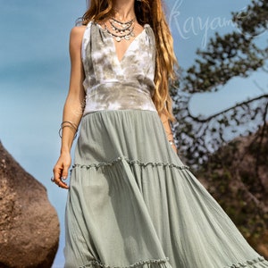 Puede incluir: Una mujer lleva un vestido maxi de color verde con volantes y un top de tie-dye. El vestido tiene un escote en V y est&aacute; hecho de una tela ligera.