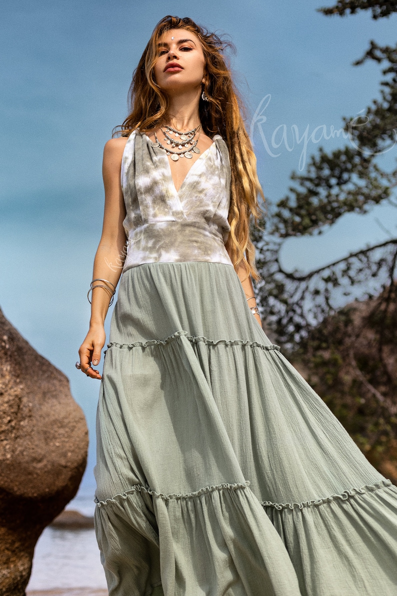 Puede incluir: Una mujer lleva un vestido maxi de color verde con volantes y un top de tie-dye. El vestido tiene un escote en V y est&aacute; hecho de una tela ligera.