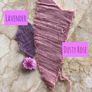 May include: Two fabric swatches, one lavender and one dusty rose, are displayed on a marble surface. The swatches are torn and frayed. A small purple flower is placed between the swatches.