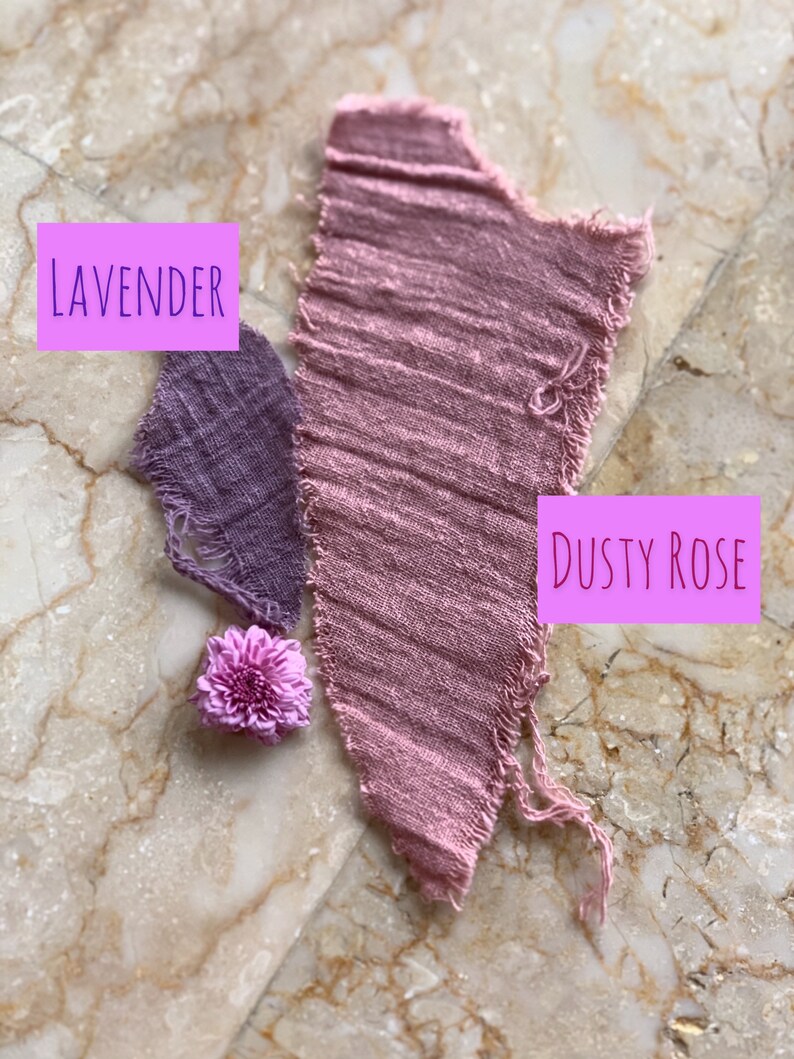 May include: Two fabric swatches, one lavender and one dusty rose, are displayed on a marble surface. The swatches are torn and frayed. A small purple flower is placed between the swatches.