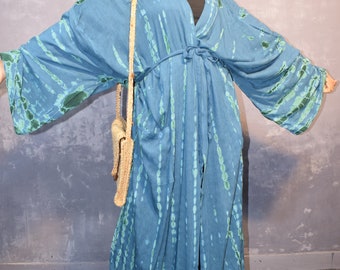 May include: A long, blue, tie-dye kimono robe featuring green vertical patterns, wide sleeves, a waist tie, and two front pockets. The garment is worn with a straw-colored woven shoulder bag and a wide-brimmed straw hat.