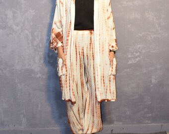 Puede incluir: Un conjunto tie-dye compuesto por un cárdigan largo de manga larga abierto por delante y pantalones holgados a juego, ambos con un patrón de rayas verticales blancas y marrones. El conjunto se lleva sobre una camiseta negra con cuello en V.