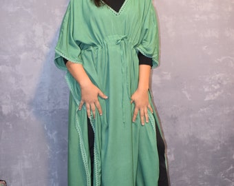 May include: A sage green kaftan dress featuring a V-neckline, short wide sleeves, and a drawstring waist. The garment is accented with decorative lace trim along the neckline, sleeve edges, and side slits, worn over a black top and black pants.
