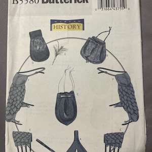 May include: A Butterick B5580 Making History sewing pattern envelope featuring illustrations of various accessories including pouches, arm guards with scale-like textures, a feather, and a belt-like piece, all labeled with letters A through G.