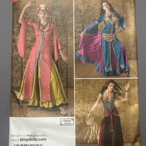 May include: Simplicity sewing pattern 2159 for costumes in sizes HH 6, 8, 10, 12. The envelope displays three variations of long dresses with flared sleeves, layered skirts, and decorative trim, featuring models in pink, blue, and black outfits.
