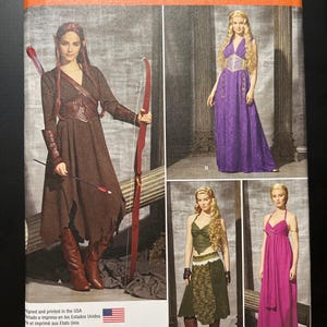 May include: Simplicity sewing pattern 1010 H5 featuring costume designs. View A shows a brown dress with a bow and arrow. View B displays a long purple dress. View C shows a long pink dress. View D features a green top and skirt set.