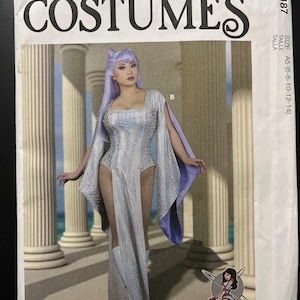 May include: McCall's Costumes sewing pattern M8187 featuring a long-sleeved, floor-length dress with a high-cut leg opening, textured silver fabric, and a purple lining. The pattern envelope displays the text McCall's COSTUMES M8187 and Yaya Han.