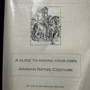 Op de afbeelding: Een wit instructieboekje met de titel Tassels and Trim, A Guide to Making Your Own Arabian Native Costume door Leslie en Michael Maurer. De omslag bevat een zwart-witte lijntekening van een persoon die op een paard in kostuum rijdt.