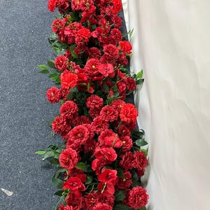 Puede incluir: Un arreglo denso de flores artificiales rojas, incluyendo rosas y otras flores, con hojas verdes. La exhibici&oacute;n floral es probablemente una guirnalda o guirnalda, adecuada para bodas o decoraci&oacute;n del hogar.