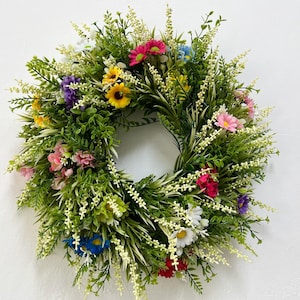 May include: A green wreath featuring a selection of colourful artificial flowers, including pink, yellow, blue and white. The wreath is made from green leaves and has a natural appearance.