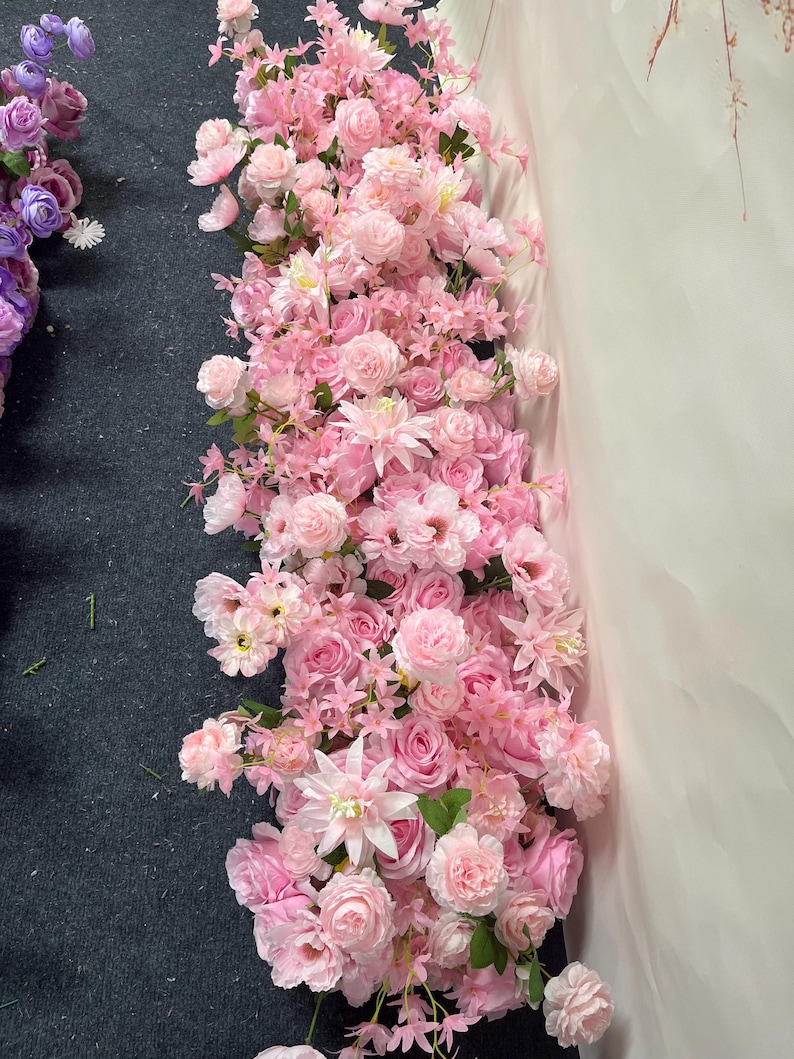 Puede incluir: Un vibrante arreglo de flores artificiales rosas, incluyendo rosas y otras flores, en cascada. Las flores var&iacute;an en tonos de rosa claro a oscuro, con hojas verdes. Adecuado para bodas u otros eventos.