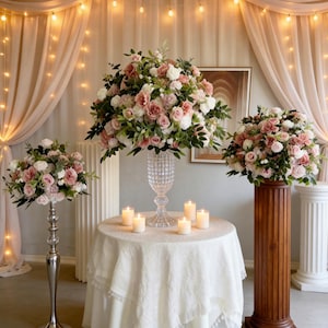Può includere: Eleganti composizioni floreali con rose rosa e bianche, esposte su un tavolo con candele e piedistalli decorativi. La scena è valorizzata da tende trasparenti e luci a catena.