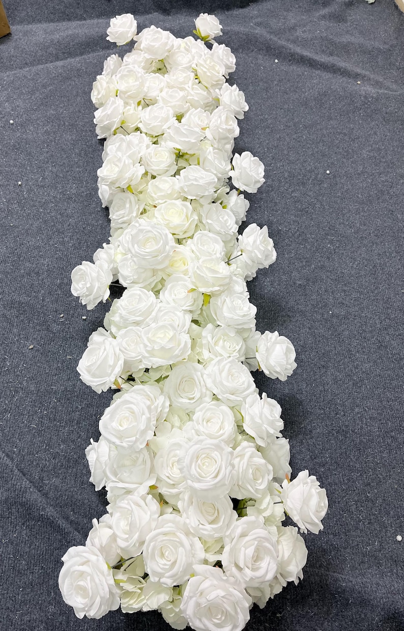 Puede incluir: Una larga y densa disposici&oacute;n de rosas artificiales blancas. Las rosas est&aacute;n muy juntas, creando una apariencia completa y texturizada. El arreglo es adecuado para diversos fines decorativos, como la decoraci&oacute;n de eventos o acentos para el hogar.