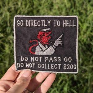 May include: A black embroidered patch with a red devil character pointing to the right. The text on the patch reads "Go Directly To Hell Do Not Pass Go Do Not Collect $200".