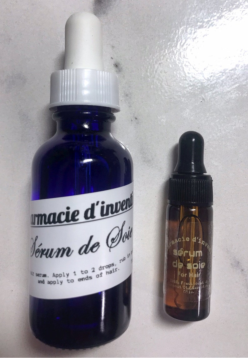 May include: Two bottles of hair serum, one blue and one amber, with dropper tops. The blue bottle has a white label with the text "armacie d'invent S&eacute;rum de Soie" and instructions for use. The amber bottle has a white label with the text "s&eacute;rum de soie For Hair".