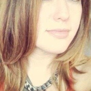 May include: A woman with long brown hair wearing a silver and black chain necklace with a pointed pendant.
