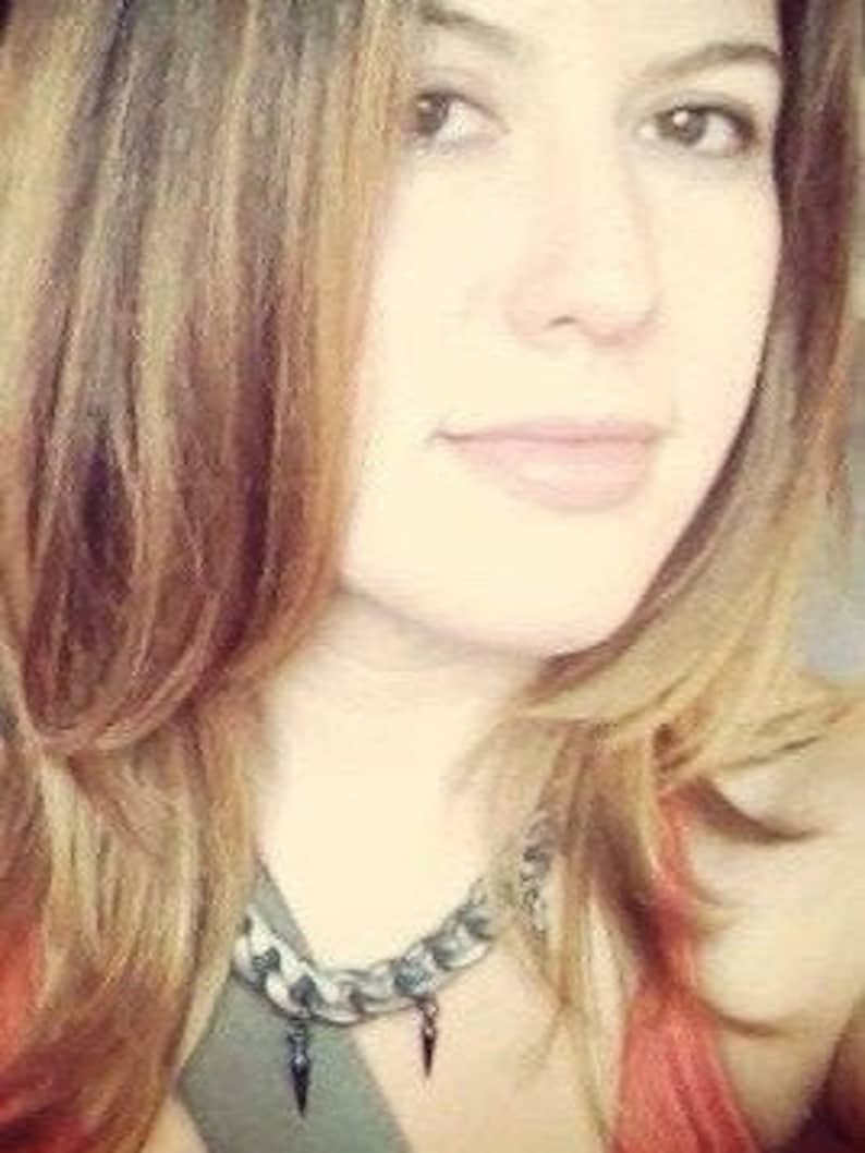 May include: A woman with long brown hair wearing a silver and black chain necklace with a pointed pendant.
