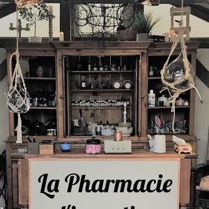 Puede incluir: Un armario de madera con estantes llenos de botellas y frascos. El armario tiene un letrero que dice "La Pharmacie d'invention".