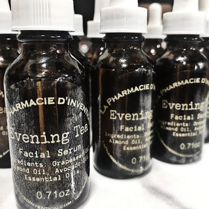 Puede incluir: Una colecci&oacute;n de botellas de vidrio &aacute;mbar con goteros blancos y etiquetas que dicen "La Pharmacie d'Invention" y "Evening Facial Serum" o "Evening Tea Facial Serum". Las etiquetas enumeran los ingredientes, que incluyen aceite de semilla de uva, aceite de almendras, aceite de aguacate y aceites esenciales. Las botellas son de 0,71 oz.