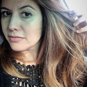 May include: A woman with long, brown hair with blonde highlights is wearing a black top with a decorative neckline. She is looking at the camera.