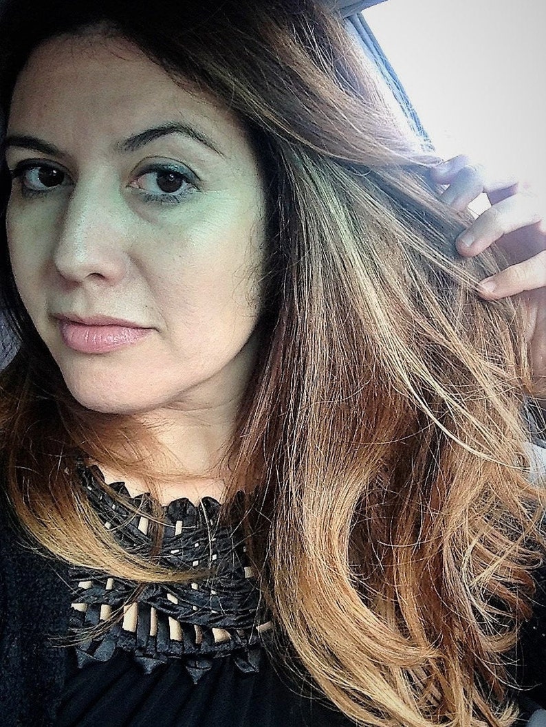 May include: A woman with long, brown hair with blonde highlights is wearing a black top with a decorative neckline. She is looking at the camera.