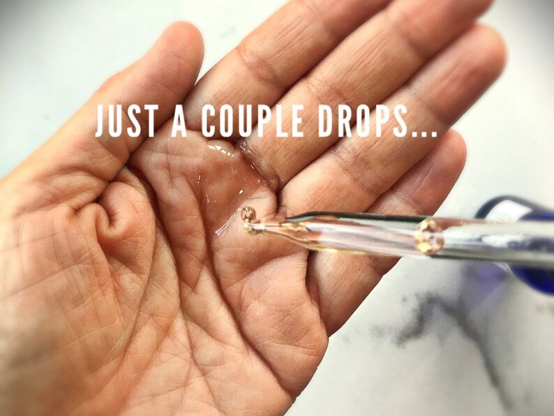 May include: A hand with a few drops of clear liquid on it. A glass dropper with a gold tip is dispensing the liquid. The text "JUST A COUPLE DROPS..." is visible above the hand.