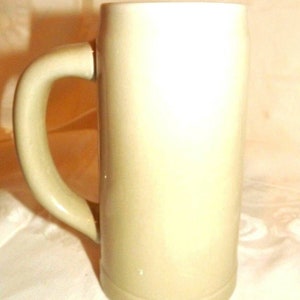 Puede incluir: Un jarro de cerveza de cer&aacute;mica beige claro sin decoraci&oacute;n, con asa. El jarro est&aacute; vac&iacute;o.