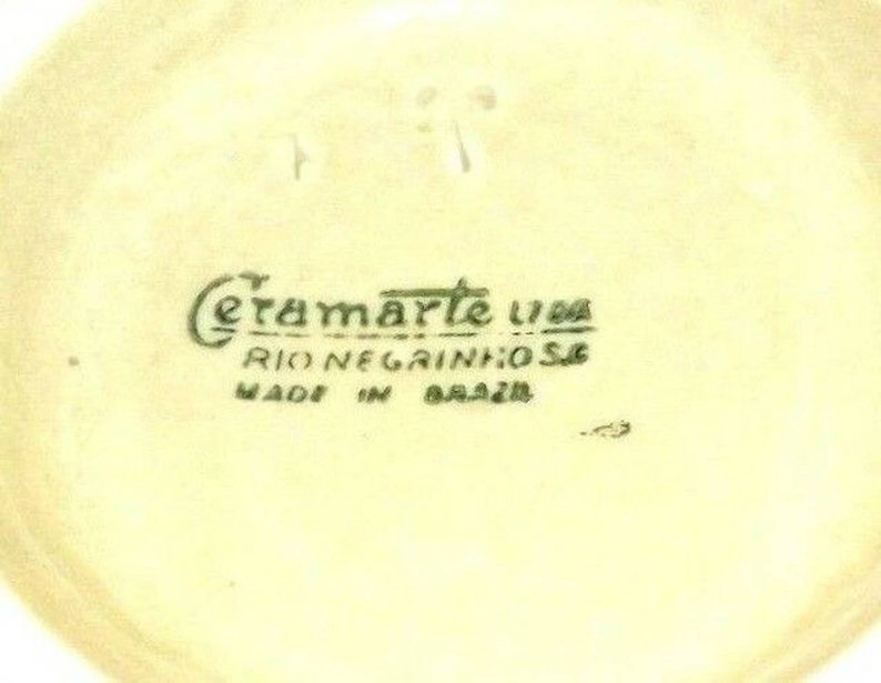 Puede incluir: Primer plano de la parte inferior de un objeto de cer&aacute;mica con el texto "Ceramarte Lda Rio Negrinhos Made in Brazil" en letras verdes.