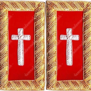 May include: Two rectangular patches featuring a red central panel with a white cross. The red panel is framed by a gold-coloured, decorative border. These patches are likely for religious or ceremonial purposes.