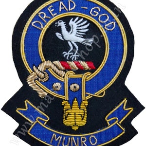 May include: A black and blue embroidered crest with a white bird, gold trim, and the text "Dread God Munro".