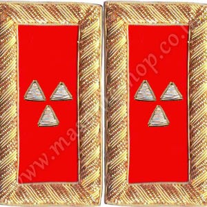 Puede incluir: Par de charreteras militares rojas y doradas. Cada charretera presenta un centro rectangular rojo con tres insignias piramidales bordadas en plata y oro. Los bordes están intrincadamente detallados con hilo dorado.