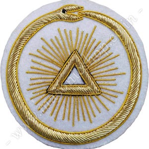 May include: A white circular patch with a gold embroidered design. The design features a snake curled into a circle around a triangle with rays of light emanating from it.