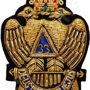 May include: A black felt patch with a gold embroidered design of two eagles with outstretched wings, a crown, and a triangle with the number 33 inside. The text "DEUS MEUMQUE JUVAT" is embroidered in gold on a blue background.