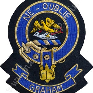 Könnte beinhalten: Ein blaues und golden besticktes Wappen mit dem Text "NE - OUBLIE" und "GRAHAM". Das Wappen zeigt einen Vogel mit einer Krone und einem Band.