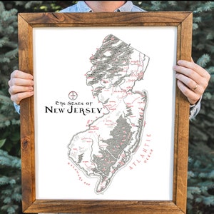May include: A framed black and white map of the state of New Jersey with red text. The map shows the state's major cities, towns, and geographical features. The text at the top of the map reads "The State of New Jersey".
