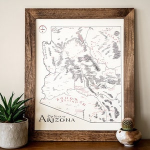 May include: A framed map of Arizona with the text "The State of Arizona" and "Sonoran Desert" in red lettering. The map is filled with black and white text and lines. The frame is brown wood.